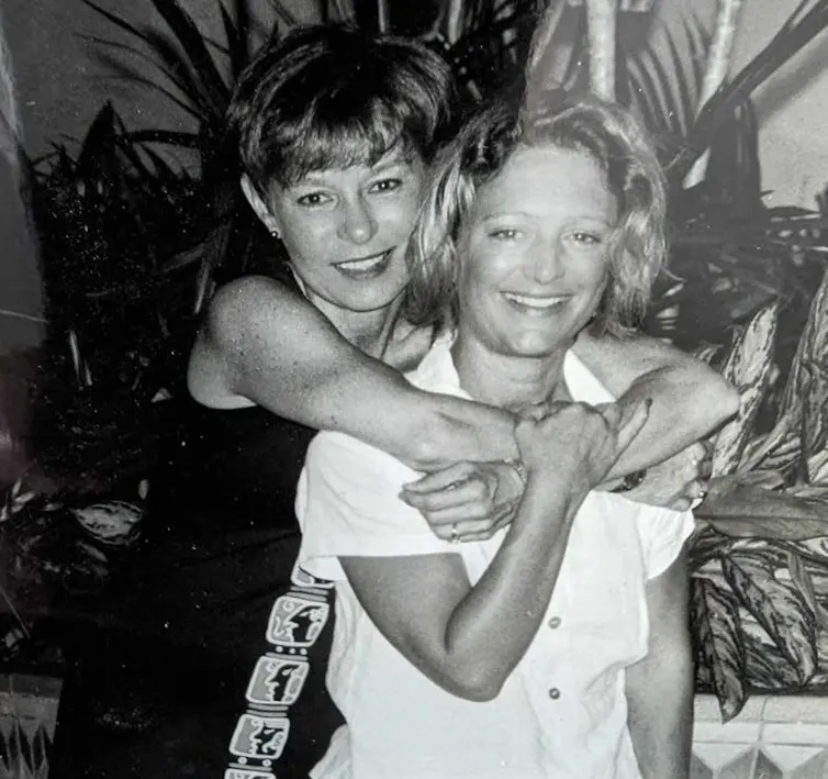 A young woman with her arms around the neck of another, both smiling