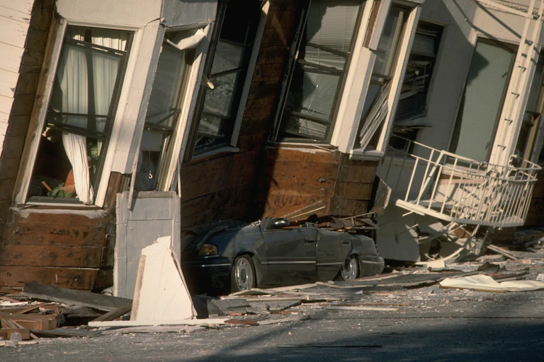 Building leaning toward viewers that collapsed into its garage and crushed a car.