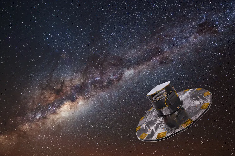A background of stars on a dark sky including the beautiful, dusty stripe of the Milky Way. In the bottom left quadrant is the Gaia spacecraft. It looks like a top hat with a wide brim. It’s mainly silver in colour with gold patches.