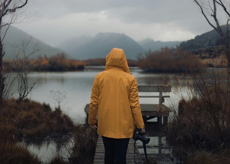 a person in a yellow raincoat looks at a body of water