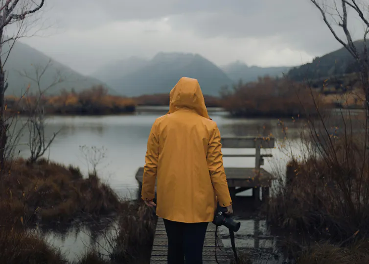 a person in a yellow raincoat looks at a body of water