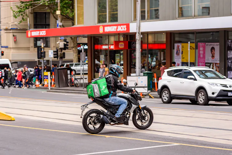 Delivery driver on a motorbike crosses tram tracks in Melbourne traffic.