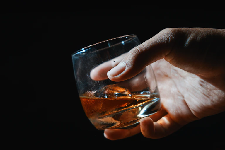 Close-up of hand holding glass of whiskey against black background