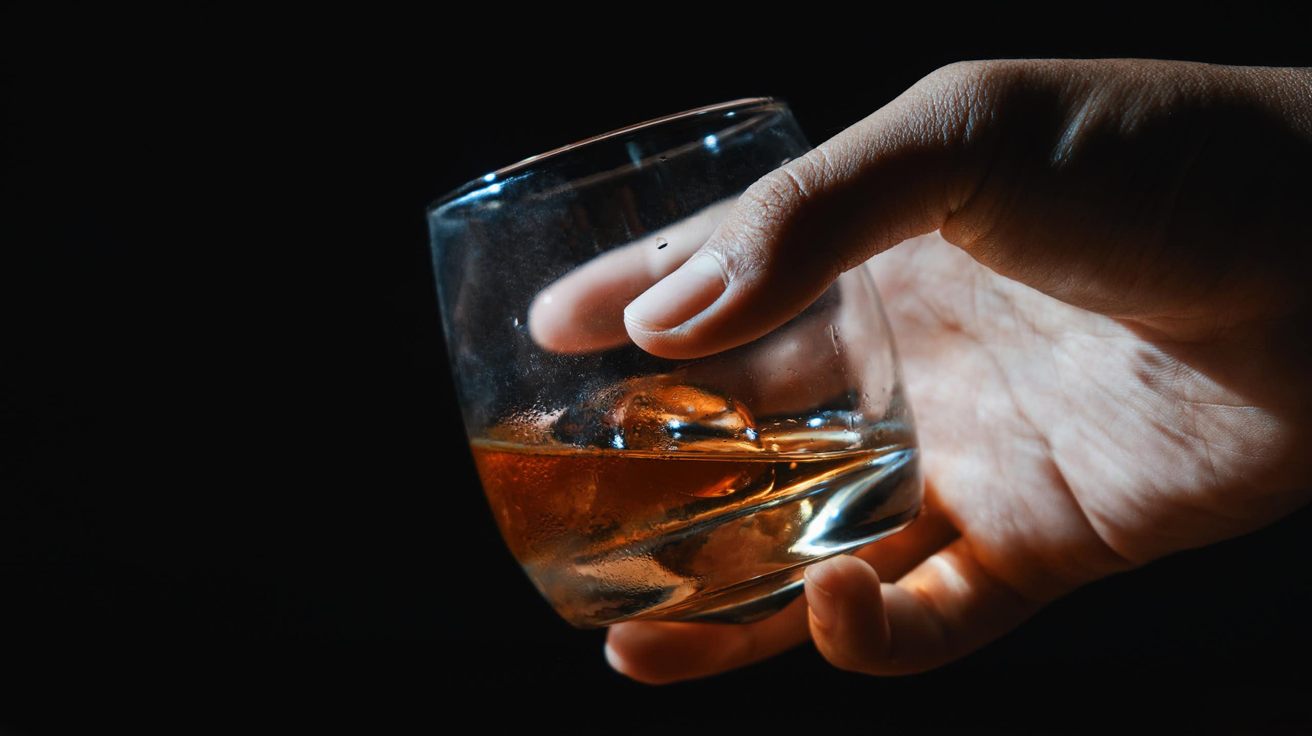Close-up of hand holding glass of whiskey against black background