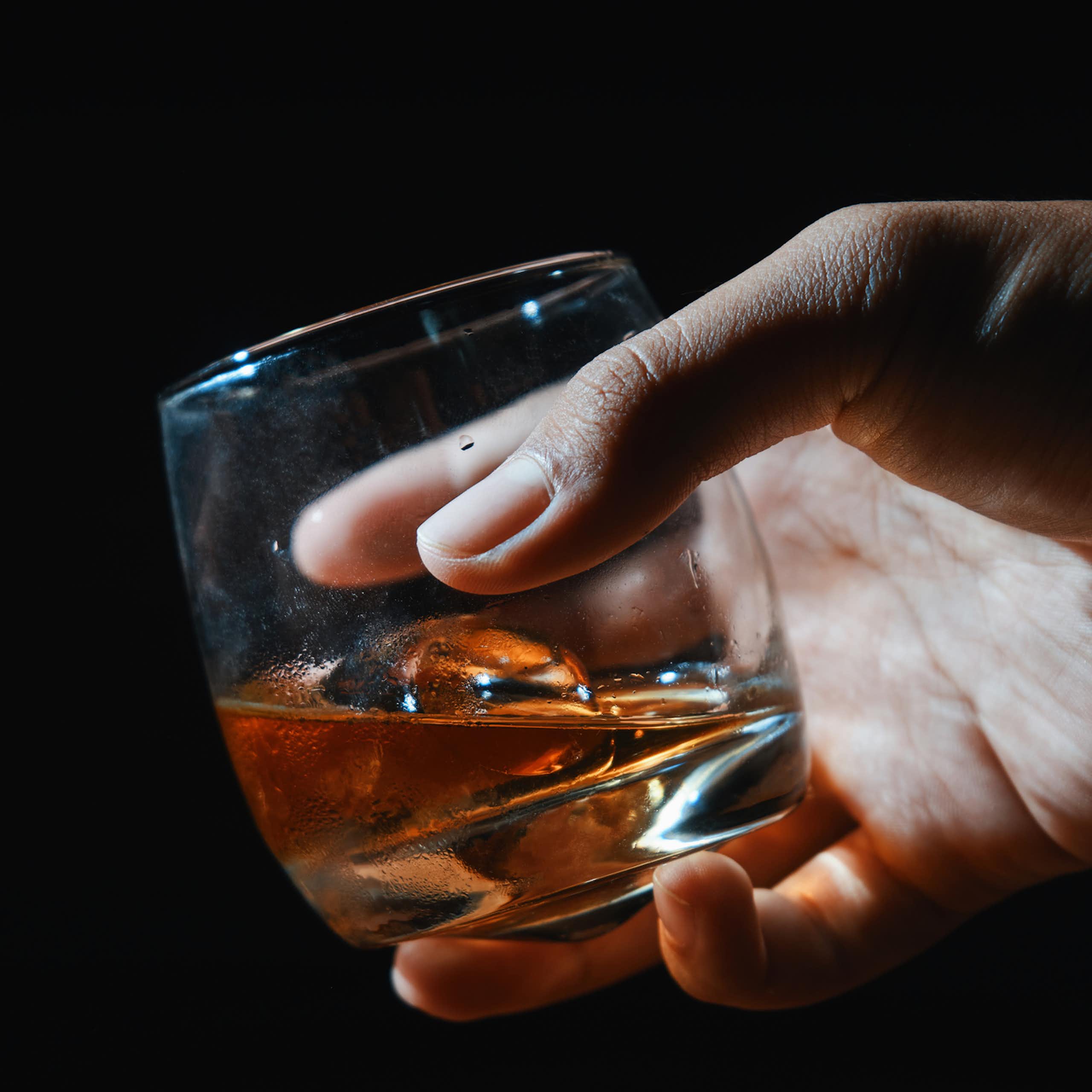 Close-up of hand holding glass of whiskey against black background