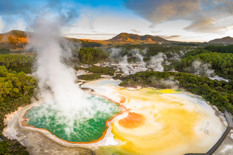 Aerial footage of hot sulphur springs at sunrise, showing colour-splashed geothermal reserve of boiling water and steam evaporating in North Island of New Zealand