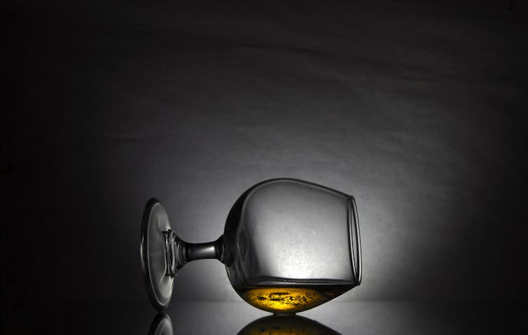 Snifter glass with amber liquid on its side against dark background