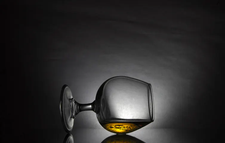 Snifter glass with amber liquid on its side against dark background