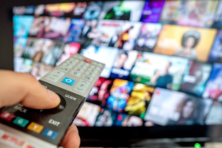 Hand hold remote control pointed at multiple video screens