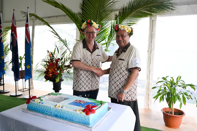 Australian Prime Minister Anthony Albanese and Prime Minister of Tuvalu Feleti Teo shake hands before cutting a cake.