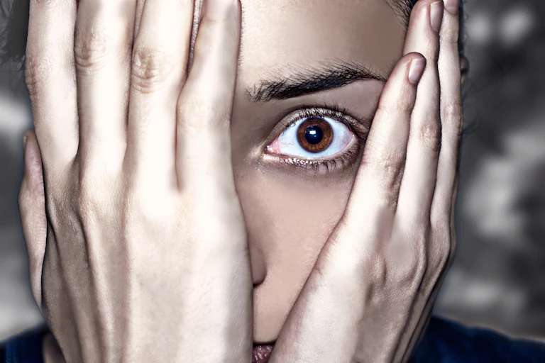 Woman looking through the hands covering the face.