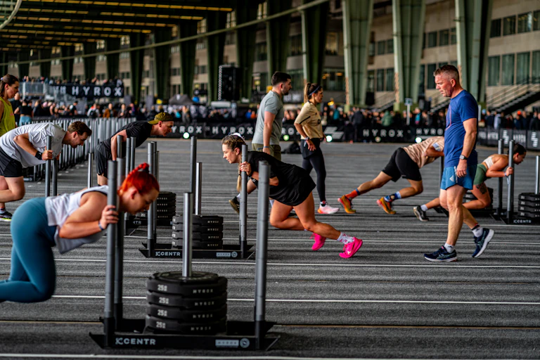 A group of Hyrox athletes push weighted sleds across a gym floor.