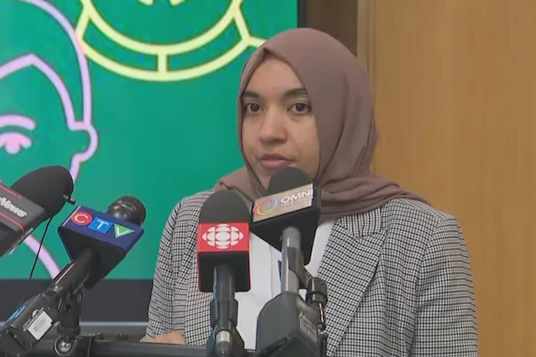 A woman wearing a hijab sits in front of four microphones.