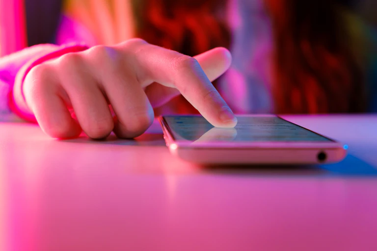 Close up of a finger scrolling on a mobile phone, cast in a pink light