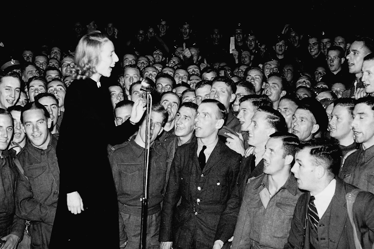 A woman on stage singing, surrounded by young solderis