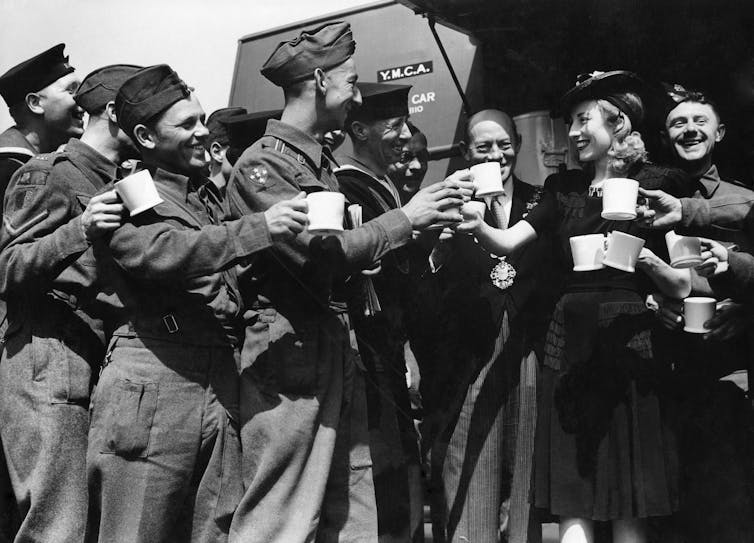 Lynn raising a cup of tea in cheers with several young soldiers.