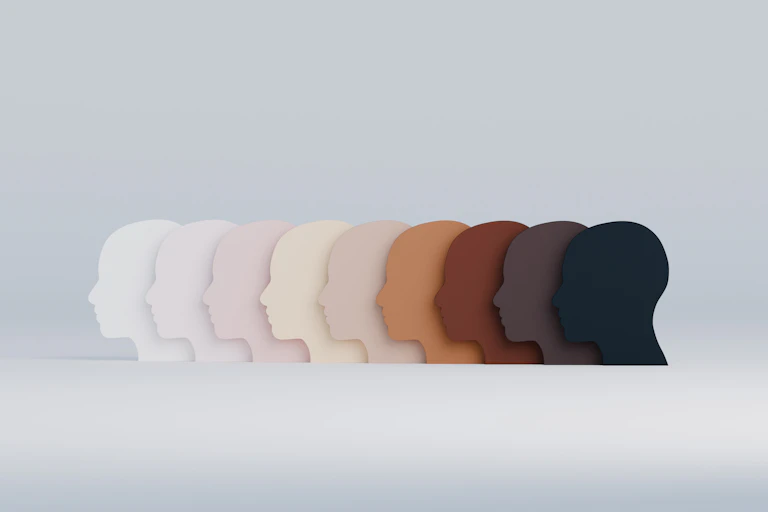 Multiple human face shapes appear in a variety of colors illustrating different races.