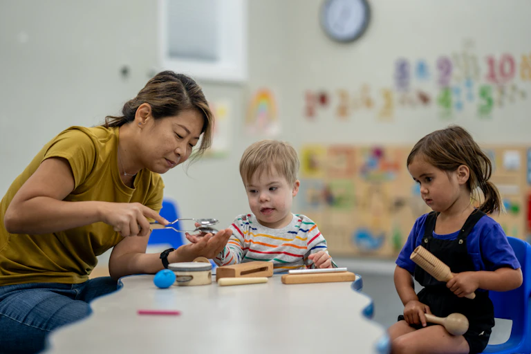 Woman sits with two small children at a table to do an activity.
