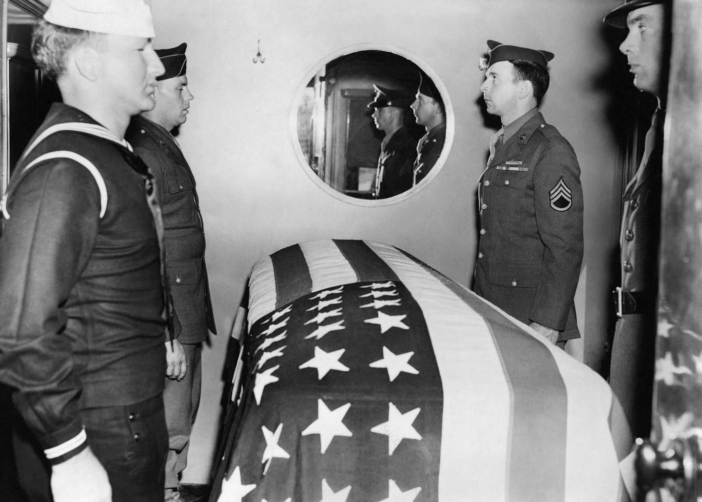 A casket draped in an American flag is guarded by servicemen.