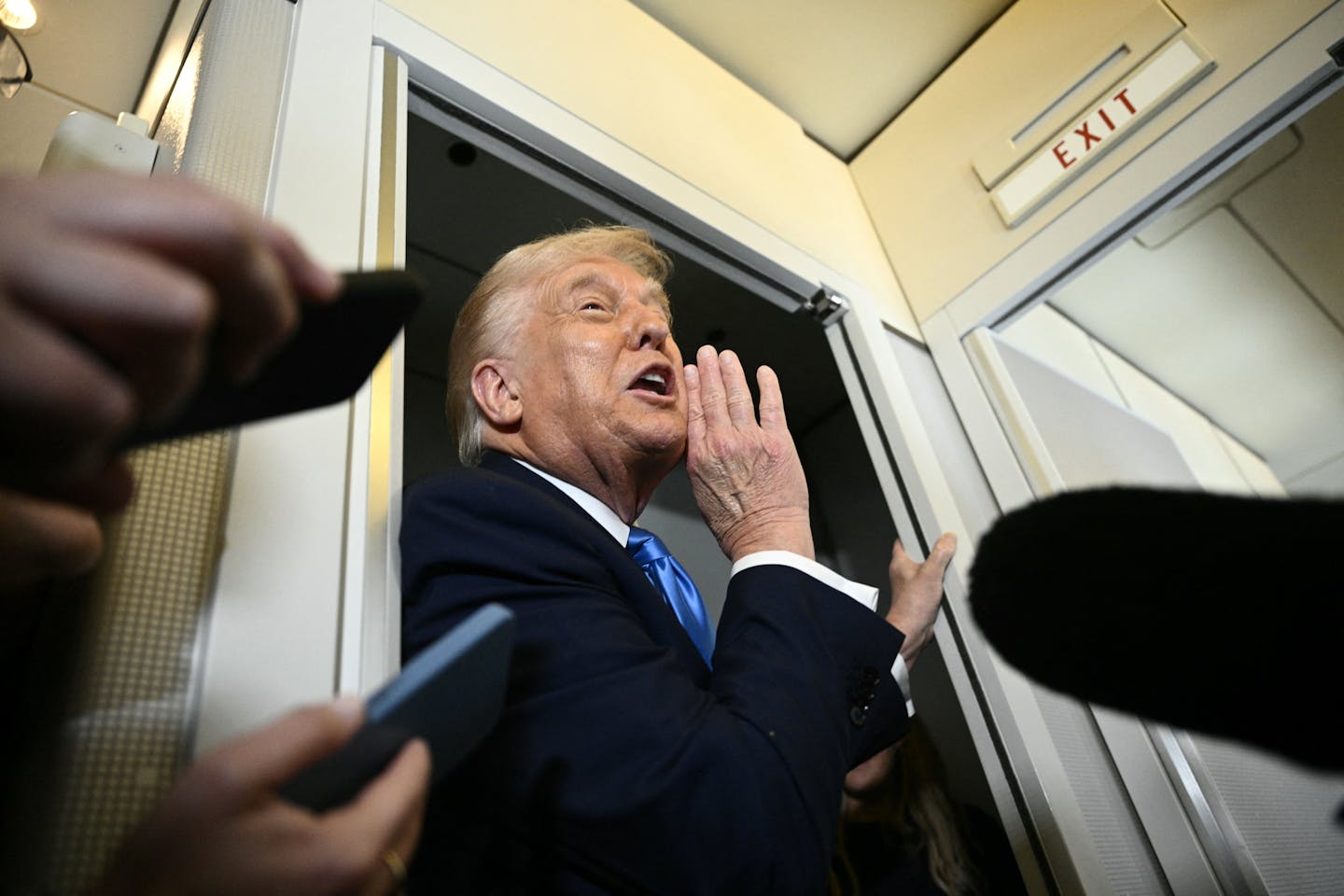 A man in a dark jacket in an airplane doorway, shouting.