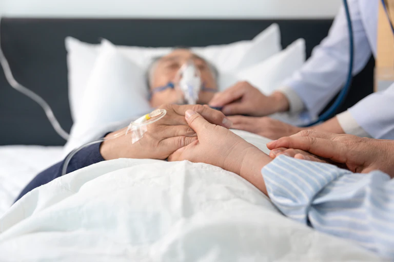 Photo d’un homme âgé intubé et allongé sur un lit, avec ses proches à côté de lui.