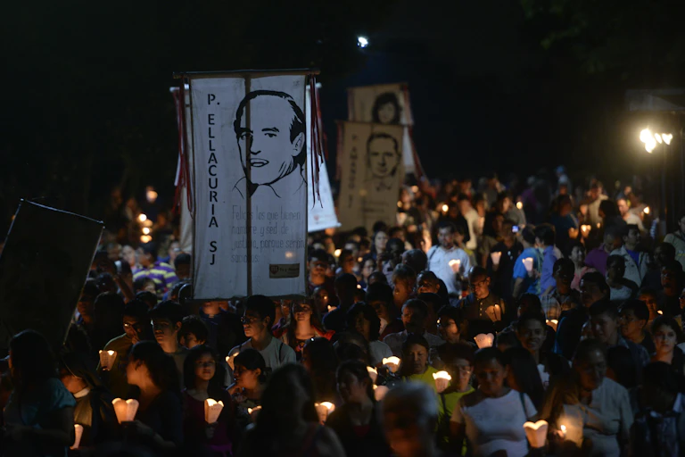 People holding candles and pancarts participate in a nighttime procession.