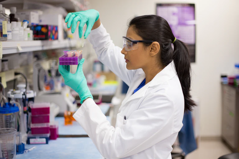 Woman in lab coat and gloves lifts vial out of tray.