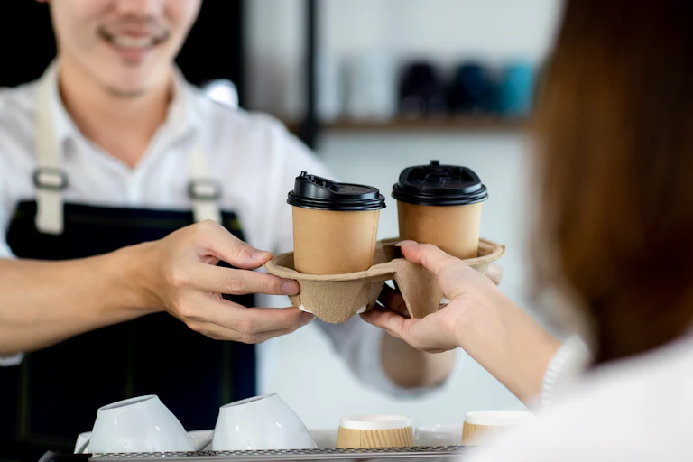 Unidentiable barista hands two take away coffees to unidentifiable customer