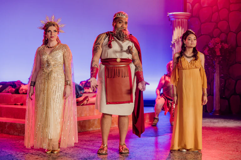 Three people on stage in a Trojan Horse musical.
