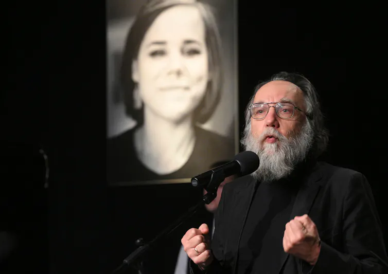 Russian philosopher Alexandr Dugin speaks into a microphone with a picture of his daughter daria in the background.