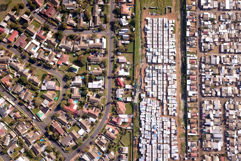 Aerial view of housing, one part well spaced with trees and swimming pools, the other part crowded with smaller buildings