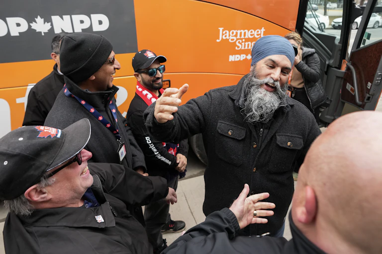 A man with a grey beard in a grey turban smiles as he talks to union members.