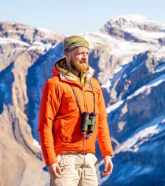 Will Hawkes, wearing orange jacket and binoculars, in mountains