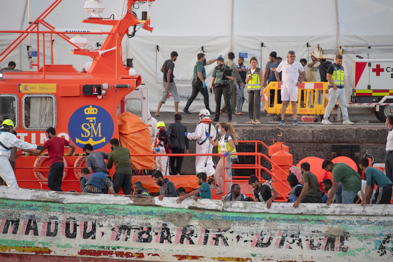 People help and prepare to help migrants who are disembarking from a boat.