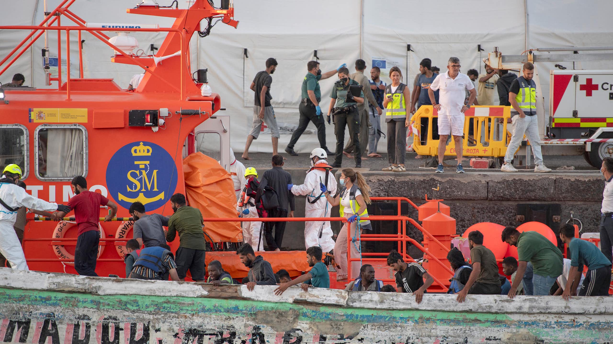 People help and prepare to help migrants who are disembarking from a boat.