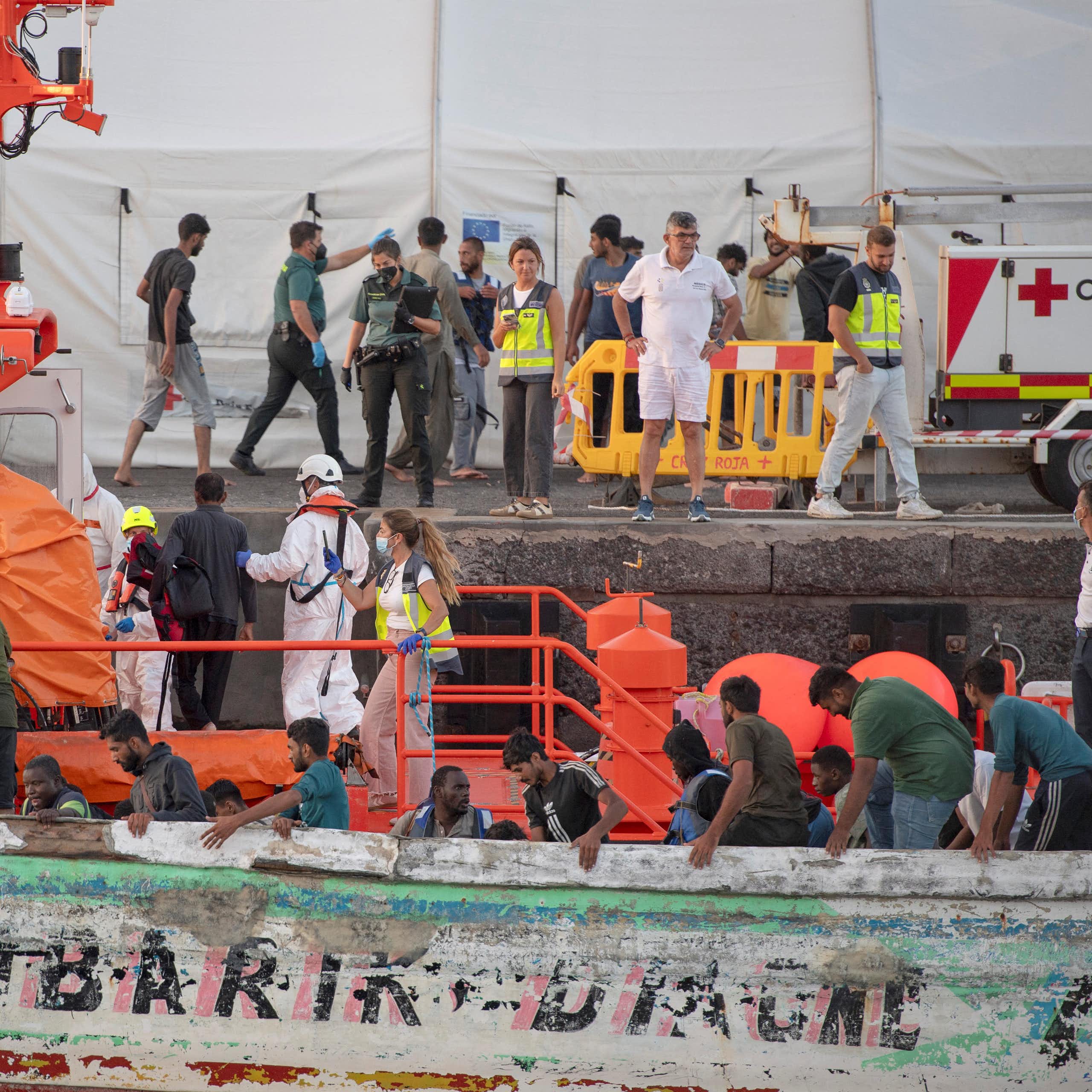 People help and prepare to help migrants who are disembarking from a boat.