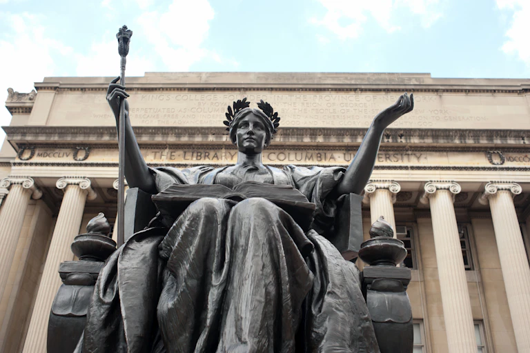 A statue of alma mater sits in front of a stone building with columns inscribed with words Columbia University.