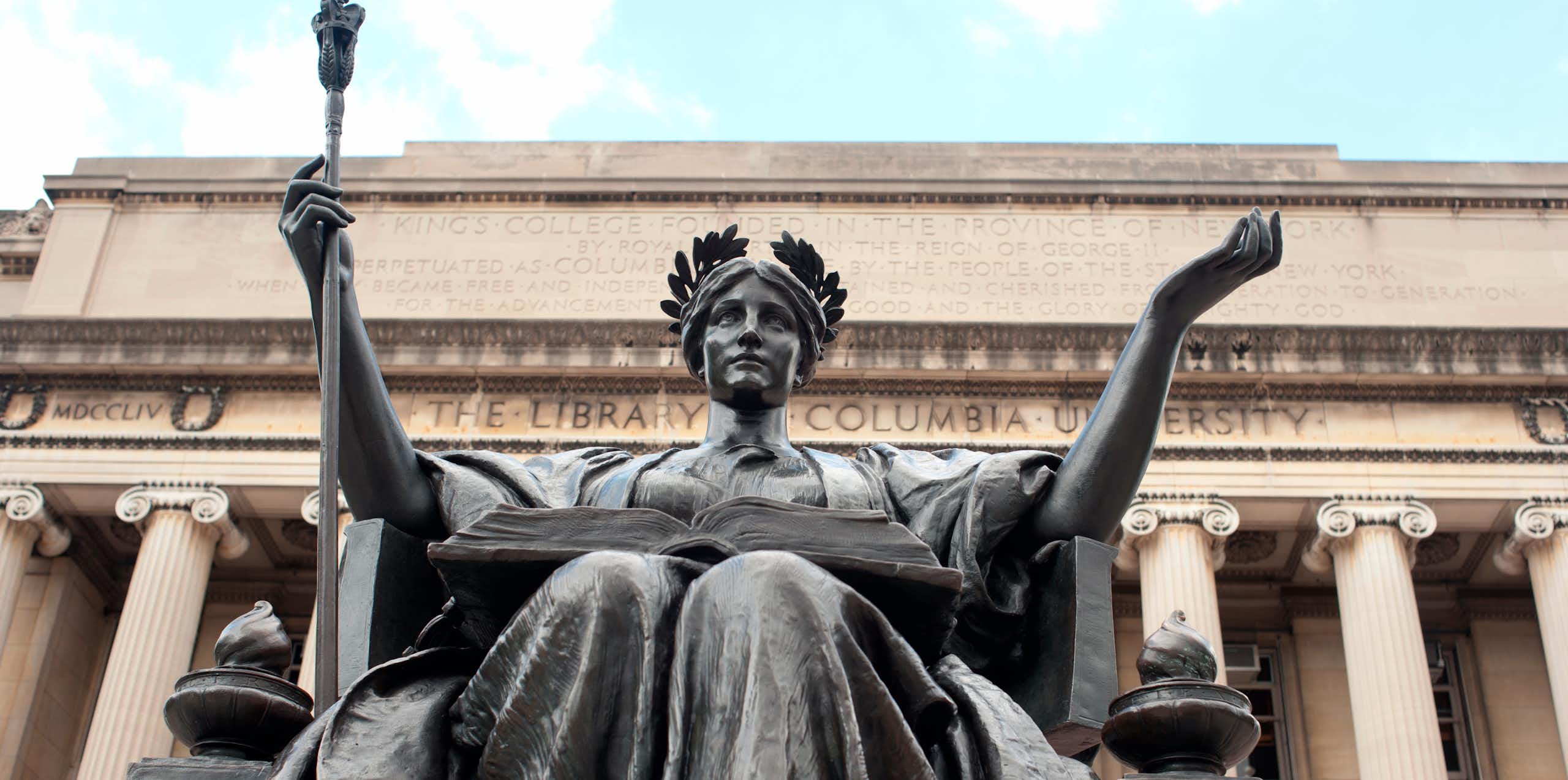 A statue of alma mater sits in front of a stone building with columns inscribed with words Columbia University.
