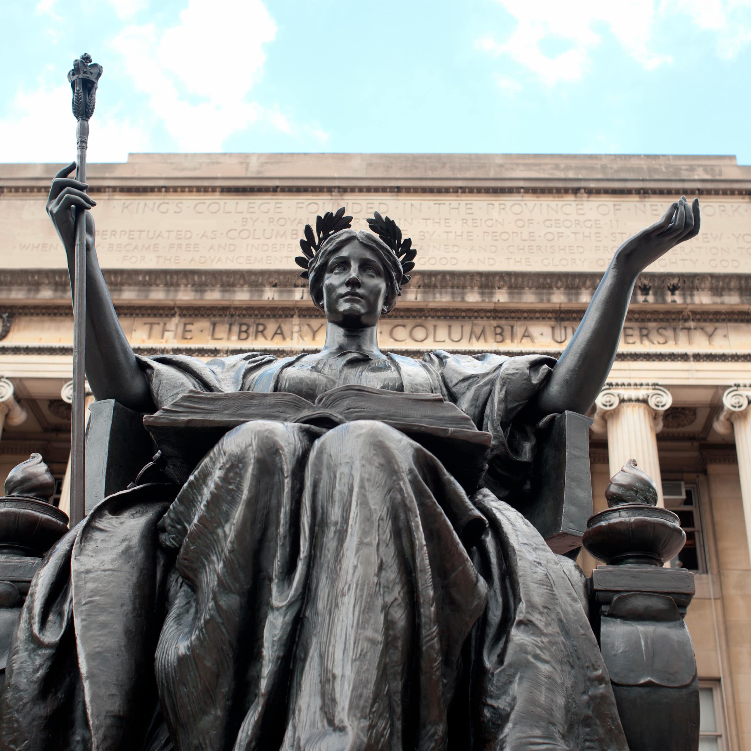 A statue of alma mater sits in front of a stone building with columns inscribed with words Columbia University.