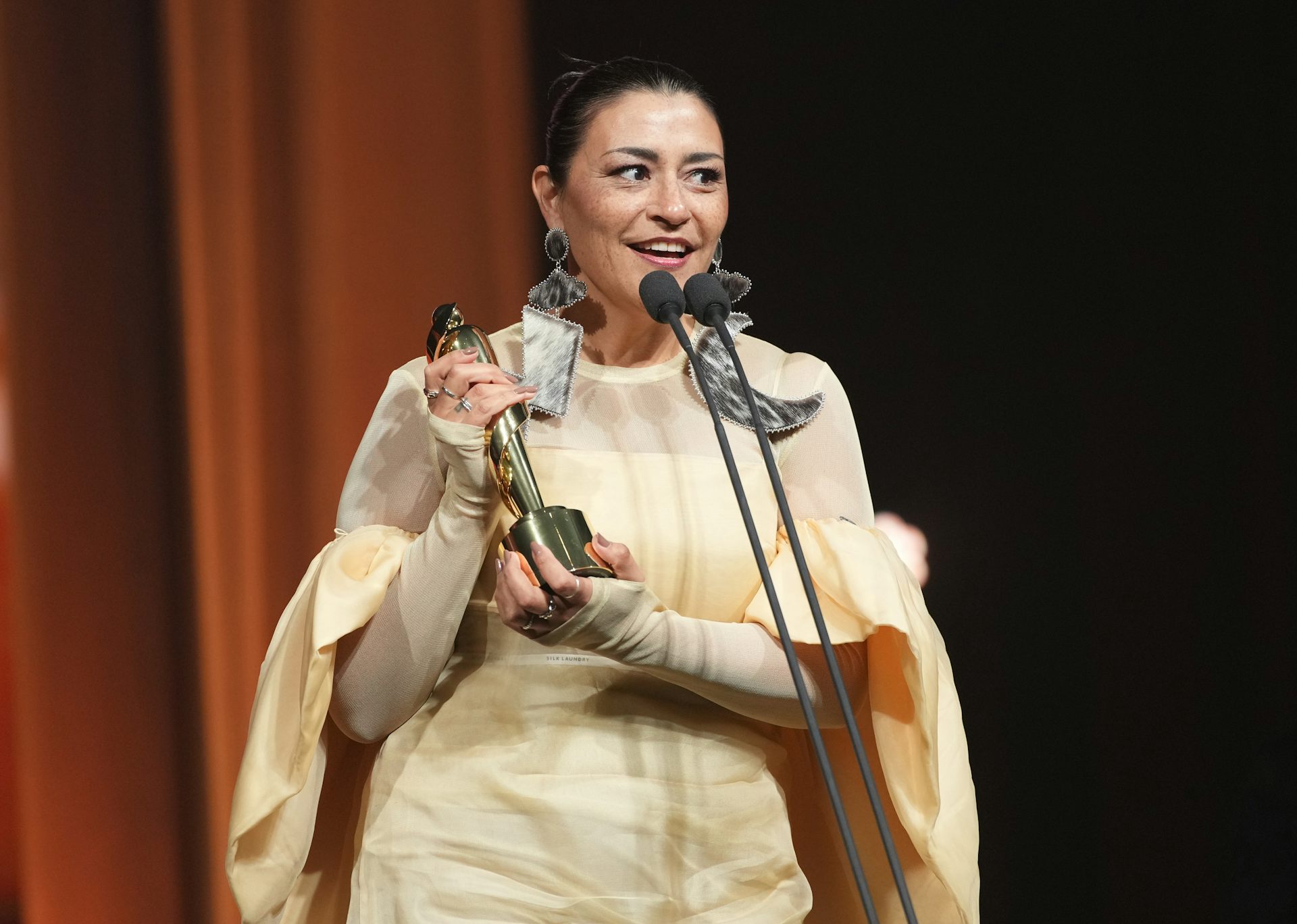 Une femme tient une statue devant un microphone.