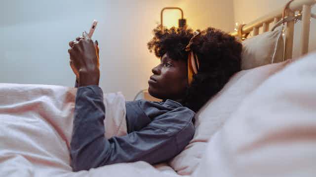 woman lying in bed looking at phone forlornly