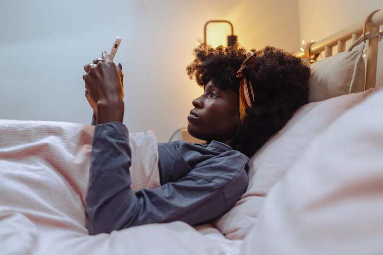 woman lying in bed looking at phone forlornly