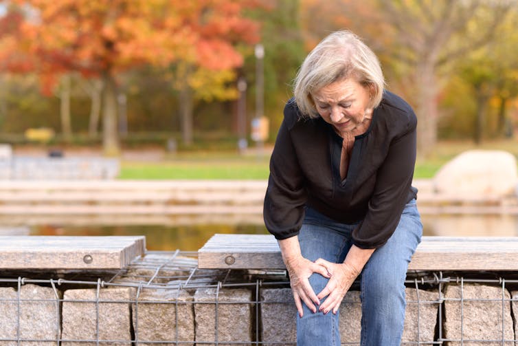 A woman sitting outside clutching her knee in pain.