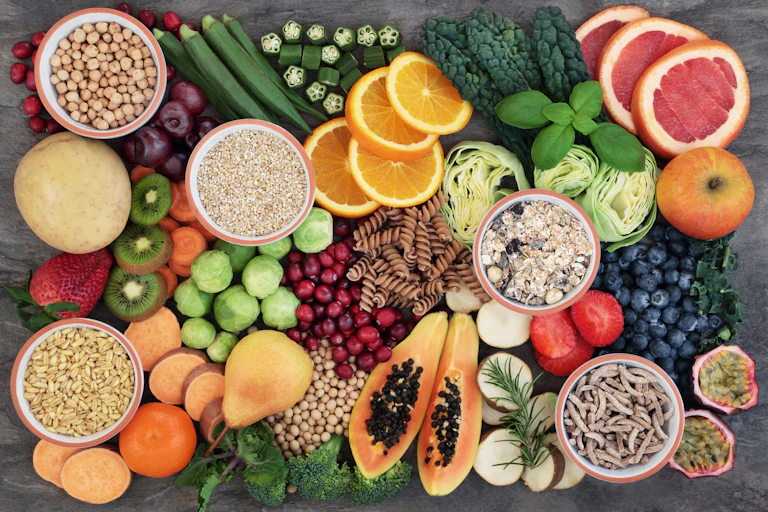 A display of fibre rich foods on a table, including papaya, kiwi, whole grain pasta and oranges.