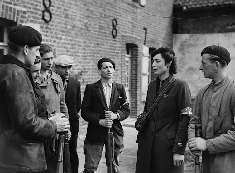 Black and white photo of group of men and a woman in conversation, some holding guns.