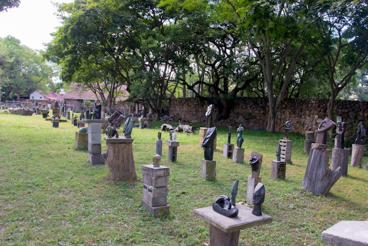 Rows of stone sculptures on a grassy lawn, trees in the background.