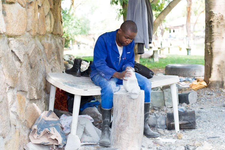 An African man in blue overalls sits as he crafts a sculpture from stone.