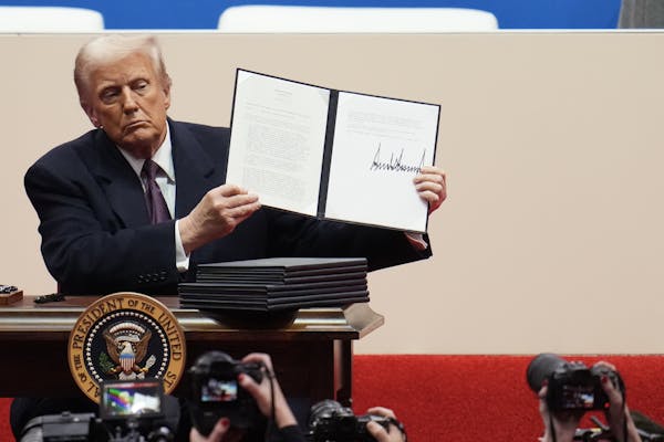 A man in a dark suit at a desk holding a folder with white pages in it.