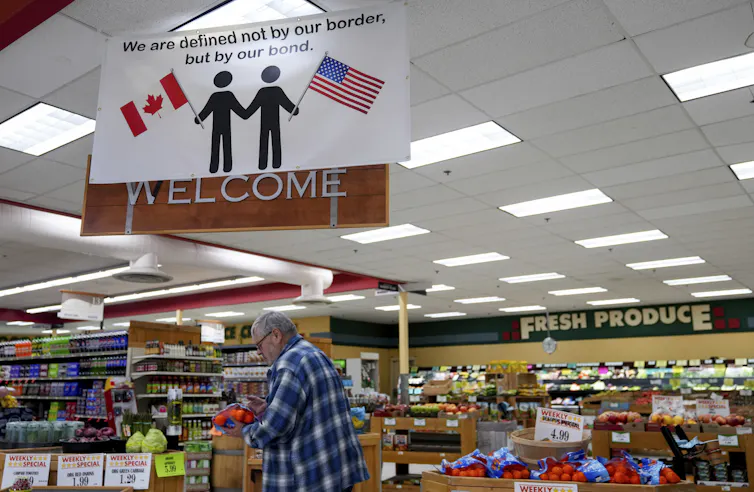 A sign extolling the Canada-U.S. relationship hangs in a grocery as a shopper inspects a bag of oranges.