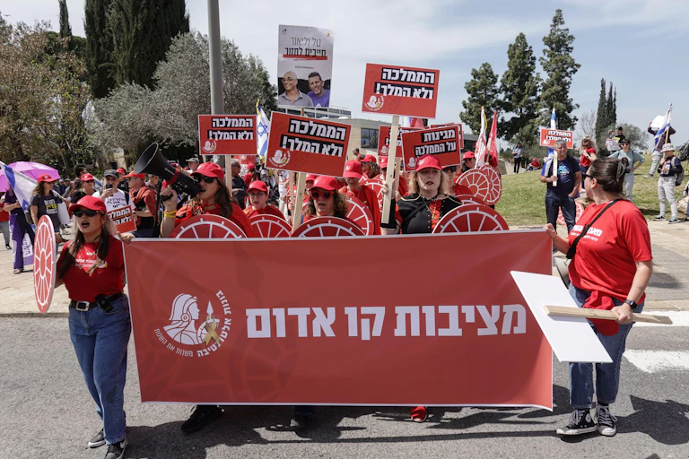 Israeli anti-government protesters wearing read t-shorts and carrying banners in Hebrew protesting against the sacking of Israel's spy chief Ronan Bar.